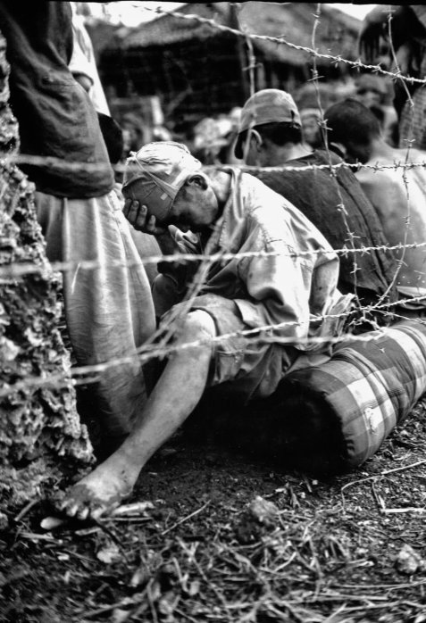 Au centre, un homme assis se tient la tête, derrière des barbelés. C'est un prisonnier de guerre, capturé pendant la bataille d'Okinawa en juin 1945.