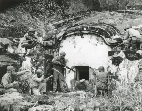 Des soldats armés de fusils entourent un caveau traditionnel d'Okinawa en forme de carapace de tortue. Ils vérifient qu'il n'abrite aucun militaire ennemi.