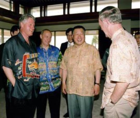 Quatre hommes debout échangent en riant. Le plus à gauche est Bill Clinton, alors président des Etats-Unis. Il porte une chemise kariyushi noire avec un motif de dragon.