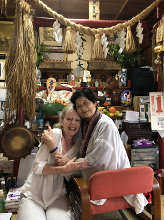 Deux femmes assises de face s'enlacent devant un autel chargé d'objets dévotionnels.