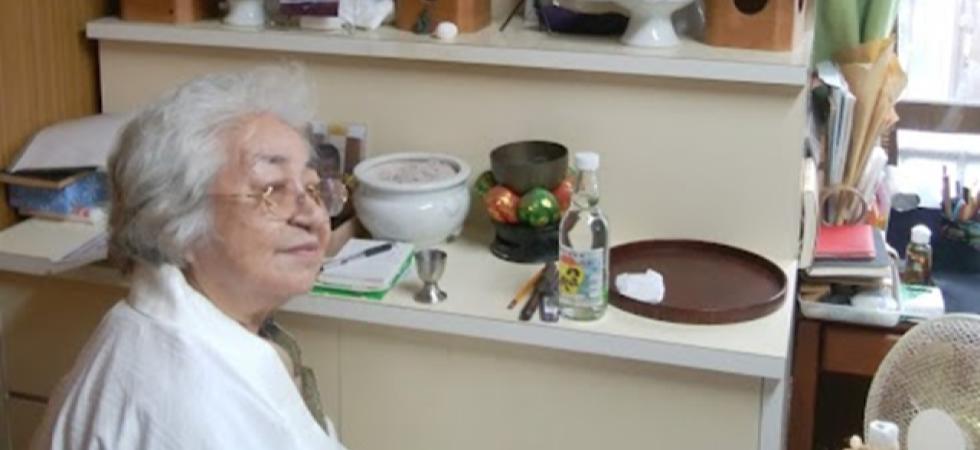 Une femme âgée de profil se recueille agenouillée devant un autel chargé d'objets dévotionnels