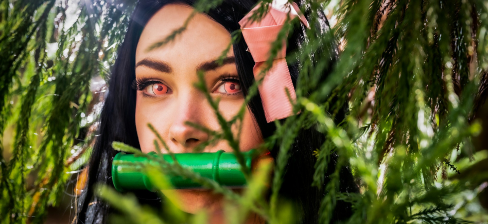 Cosplay de Nezuko, une jeune femme aux yeux roses et aux cheveux bruns entourée de végétation. Issue du manga Demon Slayer (Kimetsu no Yaiba)