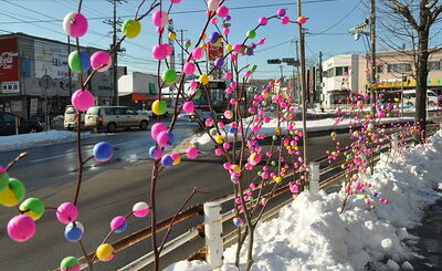 Des branches d'arbres recouvertes de mayudama colorées décorent le bord d'une rue recouverte de neige.