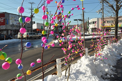 Des branches d'arbres recouvertes de mayudama colorées décorent le bord d'une rue recouverte de neige.