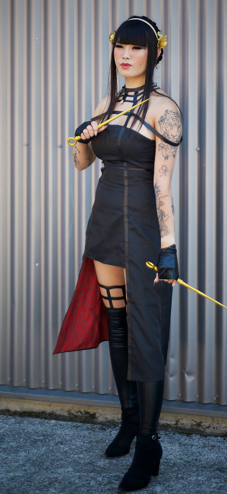 Photo d'une femme brune portant une longue robe noir et dégainant deux fines dagues dorée. C'est un cosplay de Yor Forger de SpyxFamily.