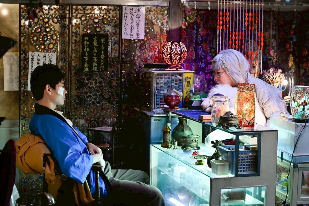 Le personnage de Kube à gauche qui consulte une voyante concernant son avenir.