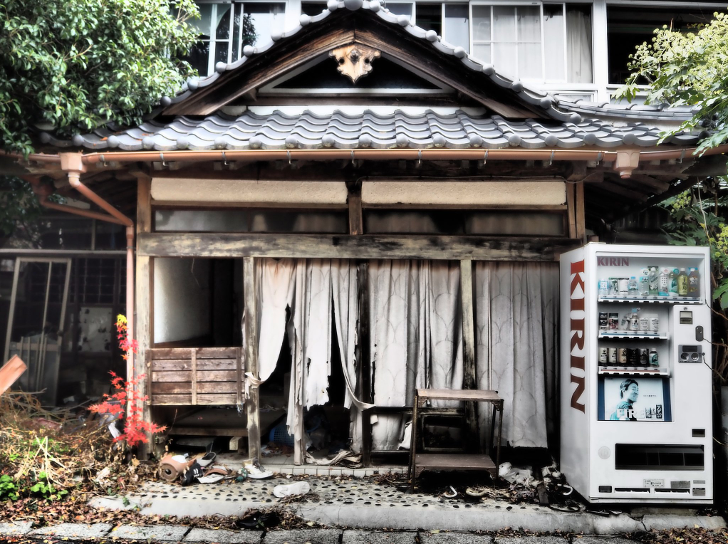 Un bâtiment abandonné dont la façade est couverte de rideaux blancs déchirés. A droite, un distributeur automatique de boissons aux couleurs passées.