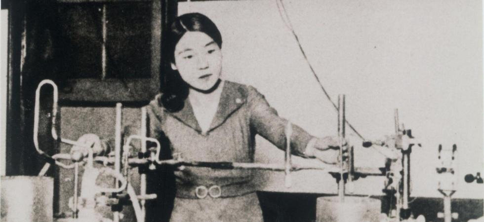 Au centre, une femme de face manipule des instruments scientifiques. Photo en noir et blanc
