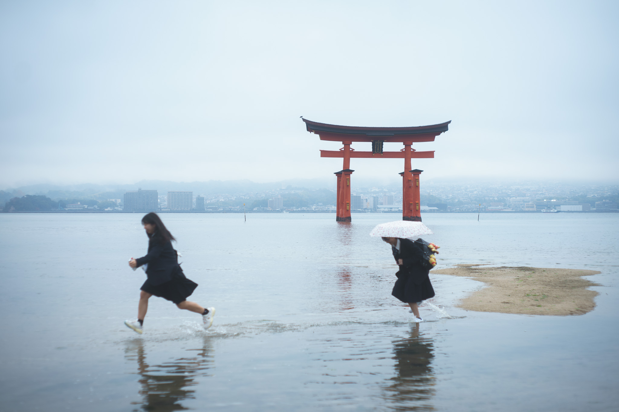 Torii flottant d'Itsukushima sous la pluie avec des écolières sous un  parapluie