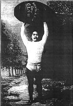 Sorakichi Matsuda soulevant un poids au-dessus de sa tête lors d’une démonstration de force.